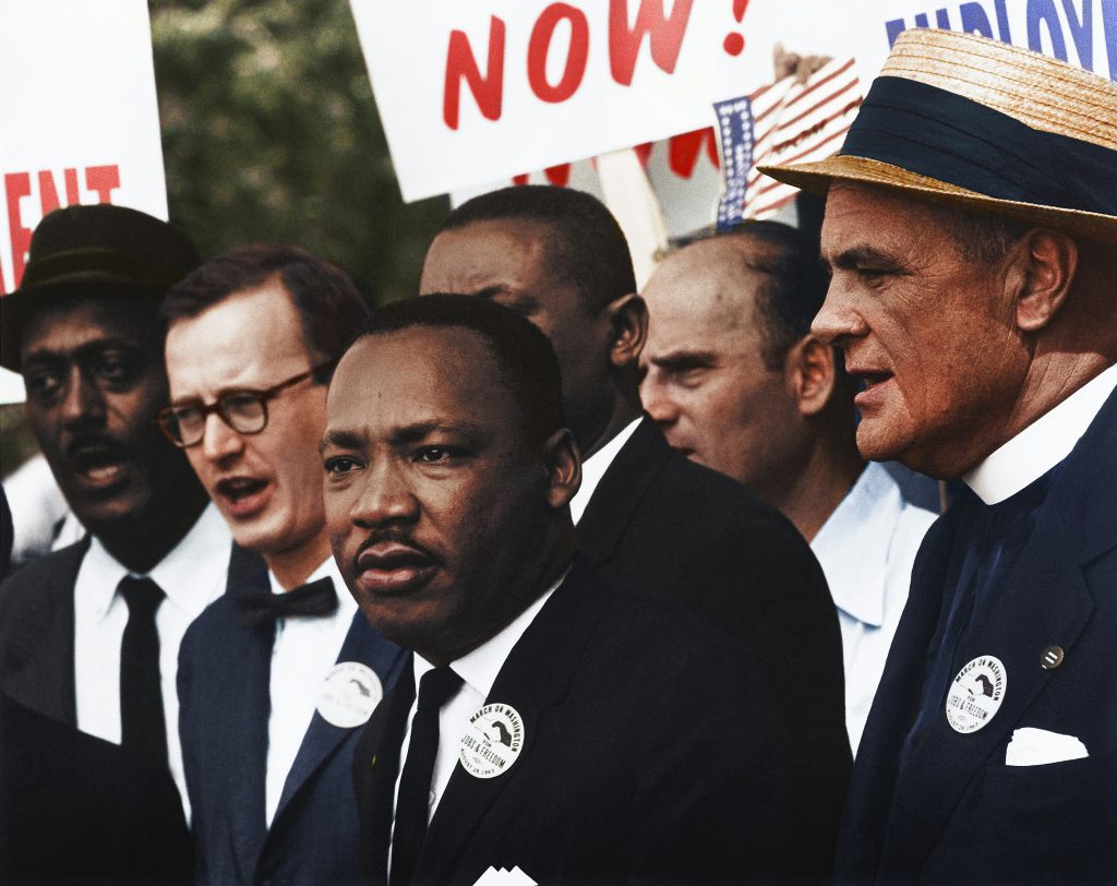 Martin Luther King Jr. stands alongside civil rights leaders and supporters during a peaceful demonstration, holding signs advocating for justice and equality.